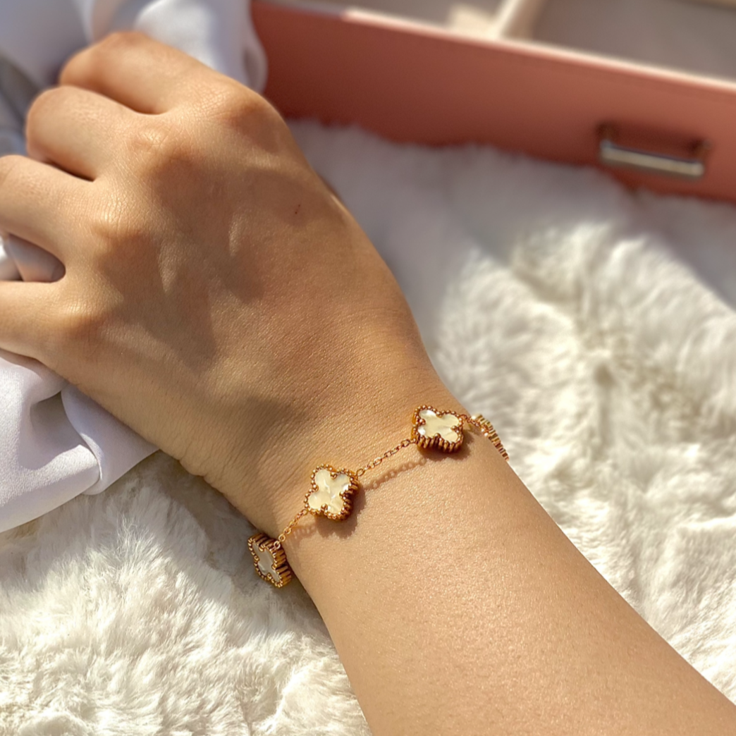 Hand wearing a gold bracelet on a white surface with a pink jewelry box in the background
